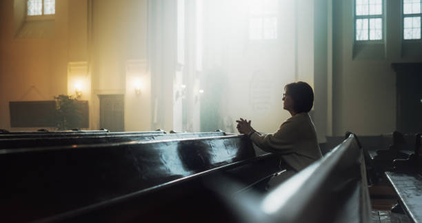 istock A Devout Christian Older Woman Sits Piously In a Church, Folding Hands For Praying, Seeks Guidance From Their Religious Faith and Spirituality. Spirit of Christianity and Belief in Goodness of God 1482224970