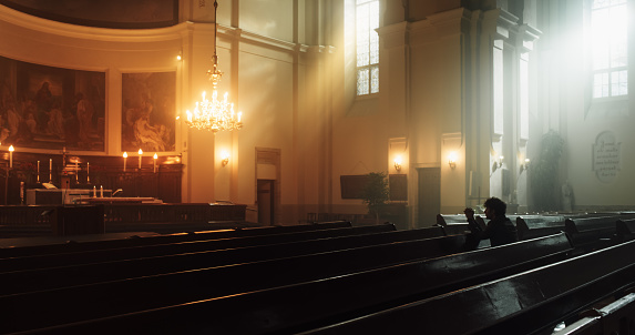 A Devout Christian Sits Piously in a Grand Old Church, Contemplating Earthly Life and Mortality. Person Seeking Moral Guidance From the Faith. Surrounded By The Peaceful Atmosphere Of The Sacred Space