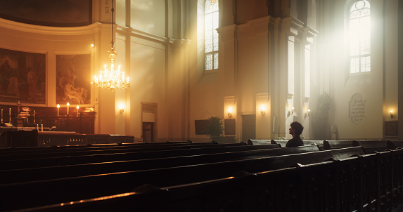 Person Sits in a Church, Praying And Feeling A Connection To God. He Believes In The Goodness And Kindness And Finds Solace In Spirituality and Religion. Contemplating Faith In Peaceful Cathedral