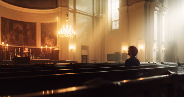 Young Christian Man Sits Piously in Majestic Church, with Folded Hands He Seeks Guidance From Their Religious Faith and Spirituality while Praying. Christianity and Belief in Power and Love of God Young Christian Man Sits Piously in Majestic Church, with Folded Hands He Seeks Guidance From Their Religious Faith and Spirituality while Praying. Christianity and Belief in Power and Love of God pentecost religious celebration photos stock pictures, royalty-free photos & images
