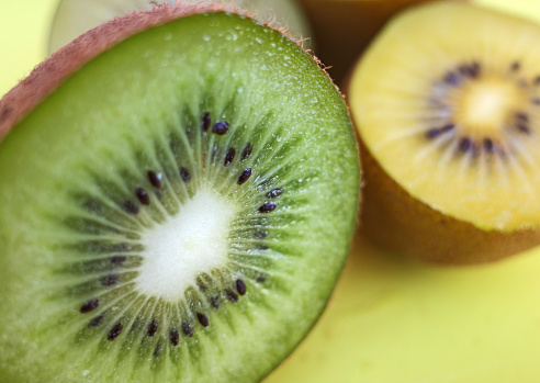 Sliced kiwis on a yellow cutting board. The yellow one is called Actinidia chinensis or golden kiwifruit. The green one is called Actinidia deliciosa or fuzzy kiwifruit