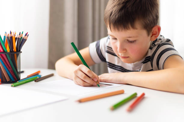 istock A child boy draws on white paper with colored pencils while sitting at a table 1482237596