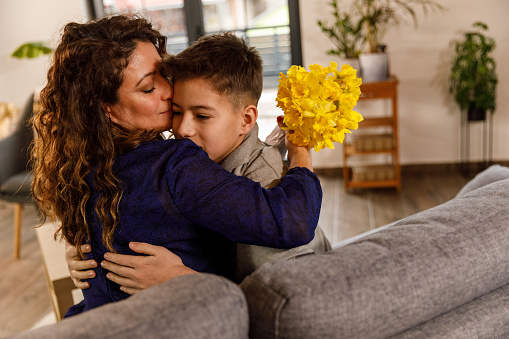 Copy space shot of happy mid adult woman and her teenage boy embracing and having bonding moments when he surprised her with a bouquet of yellow daffodils for Mother's day.