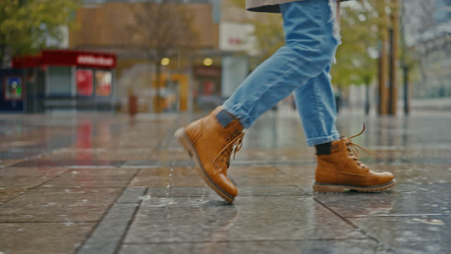 SLO MO Side view of woman's legs walking in the city on a rainy day