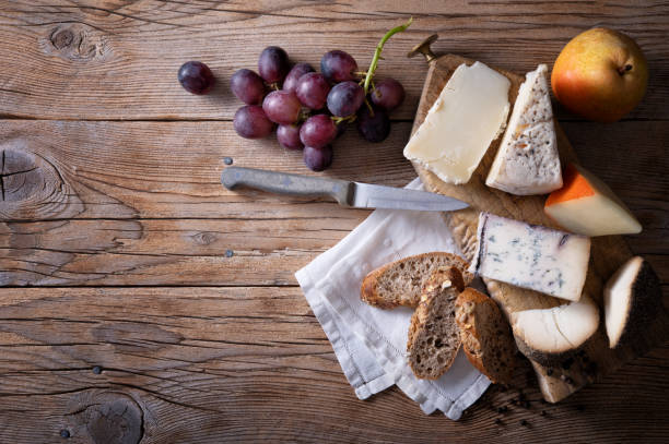 istock Italian cheese: Pecorino rosso, Blu di bufala, Pecorino toscano, Formaggio al pepe. Cheese platter, with bread, grapes and pear on wooden background, top view, space for text. 1482239030