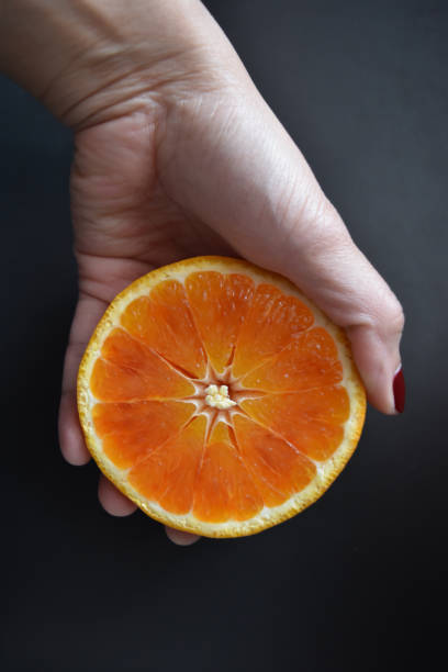 istock an Asian woman's hand holding an orange fruit against a dark background. 1482240562