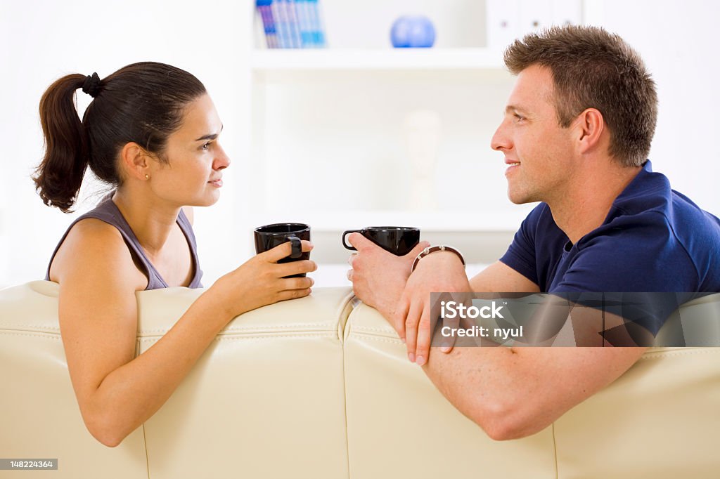 A man and woman drinking coffee on the couch Young couple sitting on a sofa, drinking, talking. Click here for more "people at home" images:  Domestic Life Stock Photo
