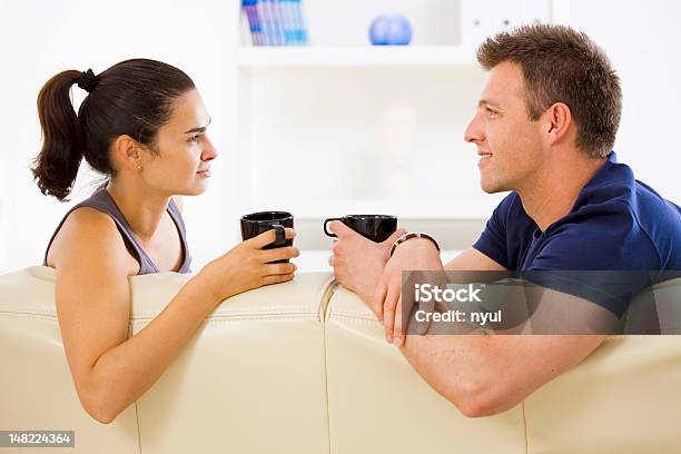 A Man And Woman Drinking Coffee On The Couch Stock Photo - Download Image Now - Domestic Life, Talking, Young Couple