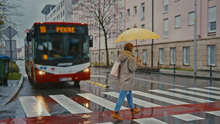 SLO MO Young woman crosses the road on a pedestrian crossing on a rainy day