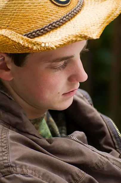 Young man in hat outdoors in cool weather on sunny day.  Eyes are downcast.