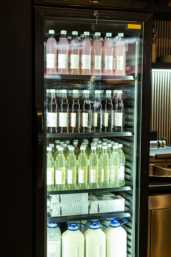 Close-up of refrigerated display cabinet with colorful soft drinks and milk in glass and plastic bottles on the metal shelves