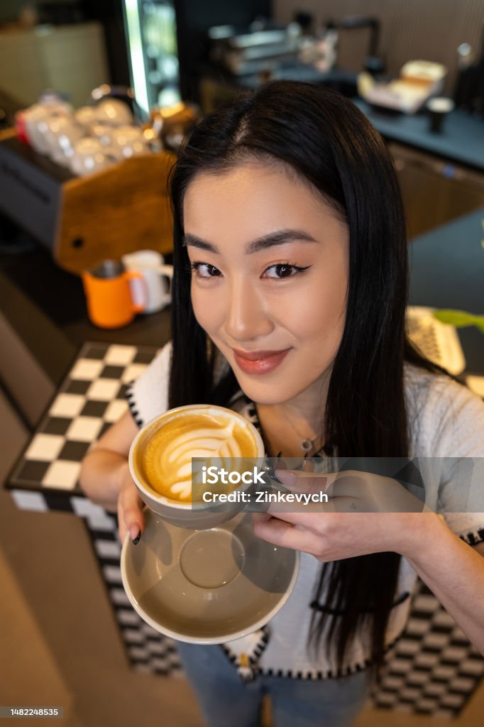 Contented cafe visitor holding a caffeinated beverage in her hand Pleased female posing for the camera with a ceramic cup of coffee and a saucer 20-24 Years Stock Photo