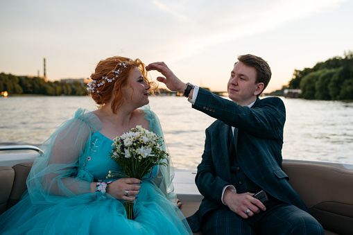 Young newlyweds couple in motor boat. Groom helping with bride's hairstyle.