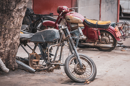 Old rusty motorcycle vehicle waste in waste scrap field with pile of old rusty metal wheels.