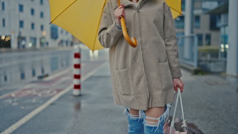 SLO MO An unrecognizable woman walks with a yellow umbrella in the city on a rainy day
