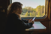 Blonde curly woman with mobile phone in hands traveling by train. Spring journey