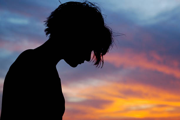 Female with head bowed in front of sunset sky