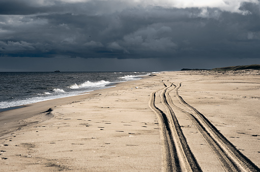 Trail of wheels of car drove along the wide sandy beach. Shore of Okhotsk sea, Sakhalin island. Dark cloudy sky