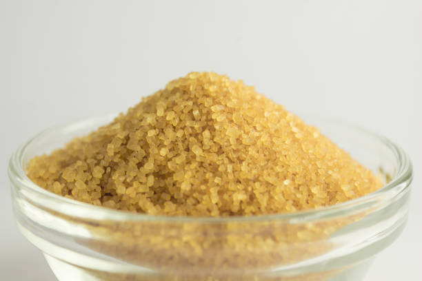 A photograph of cane sugar in a small glass bowl isolated on a white background.