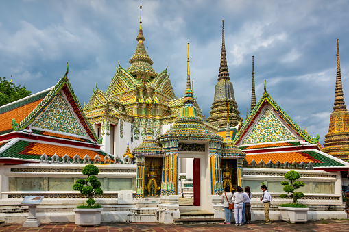 People look at a statue at Wat Pho in Bangkok, Thailand on a cloudy day.