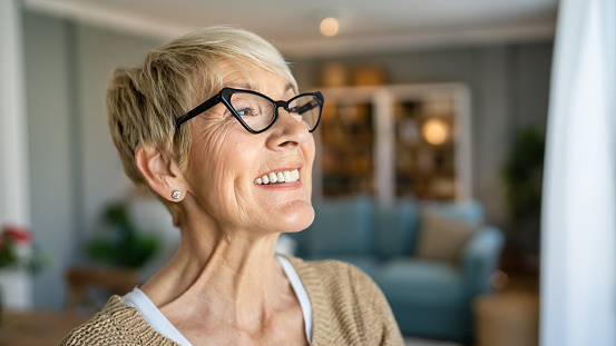Close up portrait of one senior woman with short hair happy smile positive emotion copy space standing at home indoor wear eyeglasses