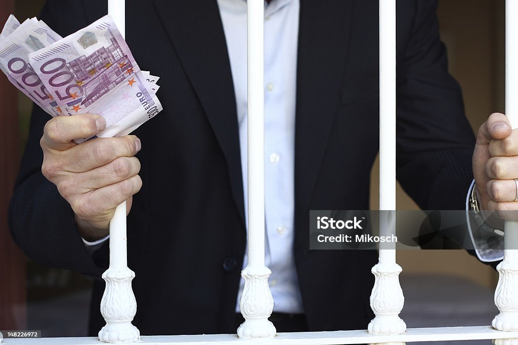 Rich behind bars A business man is trapped with lots of money behind iron bars Adult Stock Photo