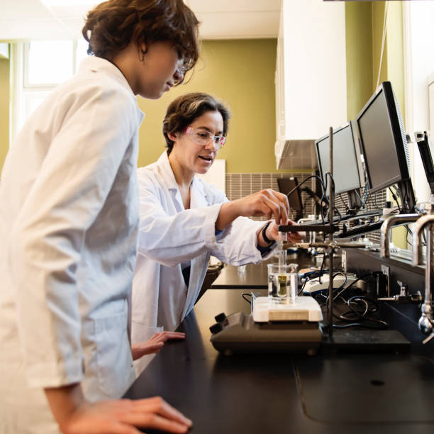Female science teacher with non-binary student in laboratory class. Female science teacher with non-binary student in laboratory classroom. She is in her thirties and is from middle-east. Student is half-asian teenager. This is part of a series promoting diversity and equity in STEM. Square waist up indoors shot with copy space.This was taken in Montreal, Quebec, Canada. nonbinary teacher stock pictures, royalty-free photos & images