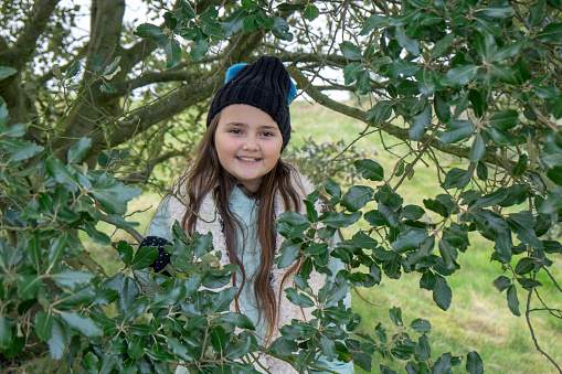 Ten year old girl in countryside pering from behind a tree