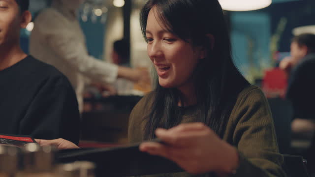 Asian woman talking with her family and choosing dinner menu in restaurant.