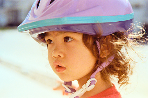 A close up of a three year old girl wearing a bicycle helmet. Scanned from a 35mm color film negative.