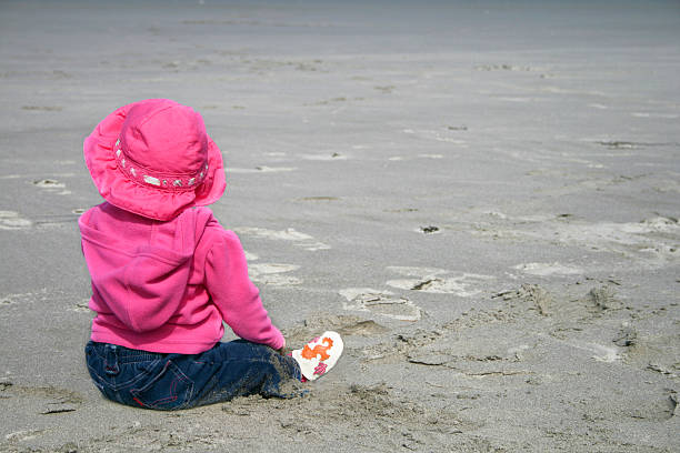 Baby girl at the Beach A baby girl dressed in a pink hat and coat enjoying a day at the beach. backside for a girl on the beach stock pictures, royalty-free photos & images