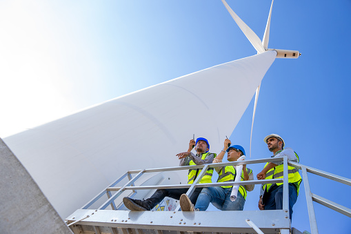 Engineer Technician brainstorming to inspect and maintenance wind turbine farm. Multi-Ethnic Blue-collar worker discussing renewable energy at windmill power generator station. Classic energy concepts