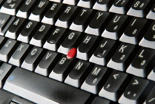 A black laptop keyboard, angled, displaying all alpha keys, minus the P. A red pointing stick is clearly visible in the center.