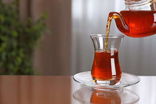 Pouring tasty Turkish tea into glass on brown table indoors, space for text