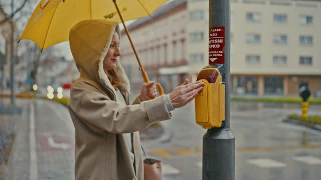SLO MO Young woman presses the button to cross the road on a rainy day