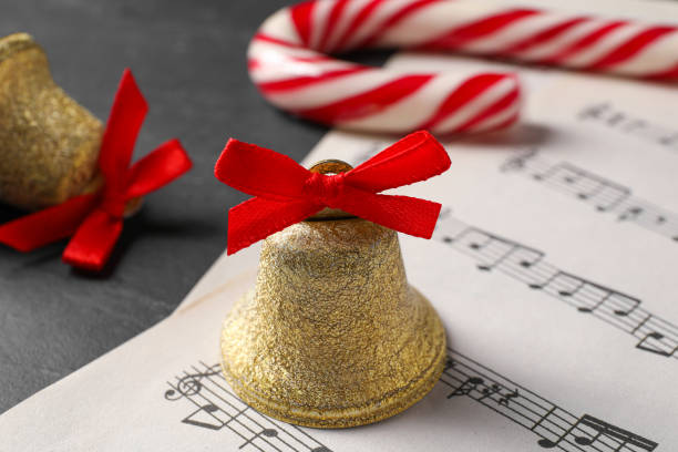 campana lucida dorata con fiocco rosso, spartiti musicali e bastoncino di zucchero sul tavolo grigio, primo piano. decorazioni natalizie - bell jingle christmas music foto e immagini stock