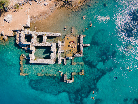 Aerial drone photo of swimmers enjoying the beautiful Kleopatra Hamamı Cove, located between Göcek and Dalaman, Turkey, known for its crystal-clear waters and ancient ruins.