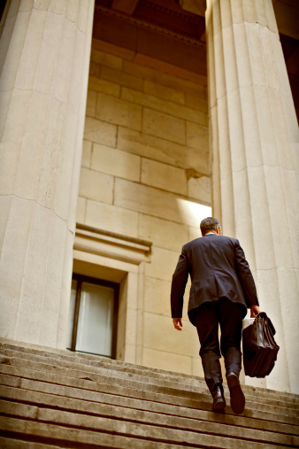 A businessman climbing steps framed by gigantic gothic pillars similar to those found outside of a courthouse or federal building.