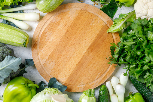 Border of green raw vegetables around empty cutting board. Top view of healthy organic food. Place for your product or text. Flat lay. Copy space.