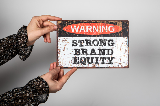 STRONG BRAND EQUITY. Warning sign with text on a white background in a woman's hand.