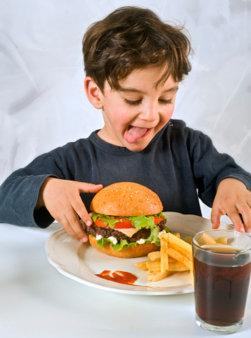 young boy eating chessburger with french fries and coke