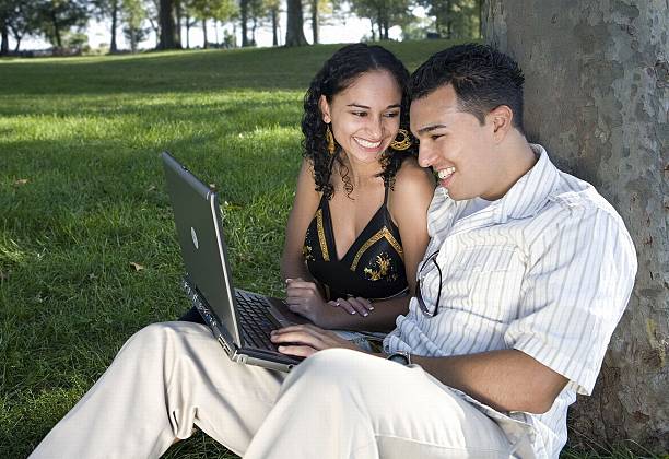 pareja joven en una computadora portátil en el parque - high key portrait color image travel locations fotografías e imágenes de stock