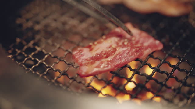 Close up grilling roasting fresh juicy meat beef slices on charcoal grill in yakiniku restaurant.