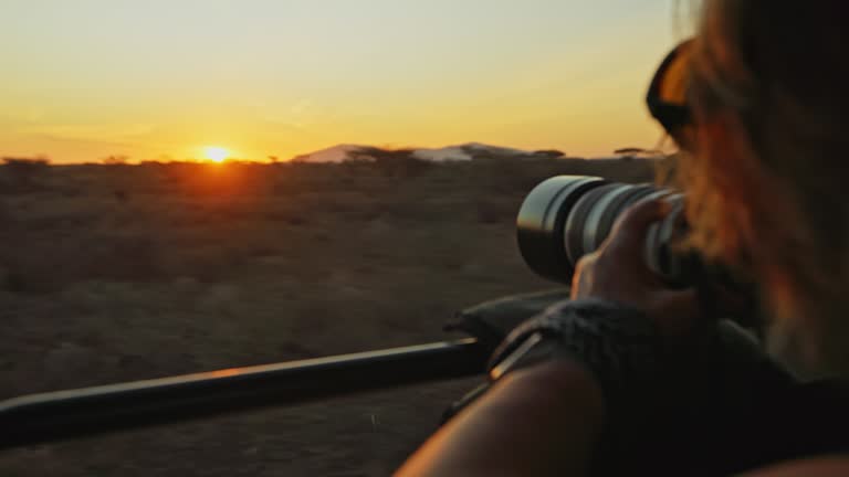 Handheld shot of woman photographing sunset. Female tourist is taking picture through camera. She is exploring desert area during vacation.