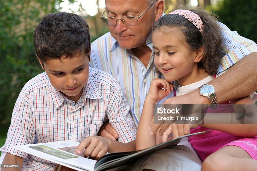 grandfather and kids reading book outdoors Grandfather and kids outdoors Grandfather Stock Photo