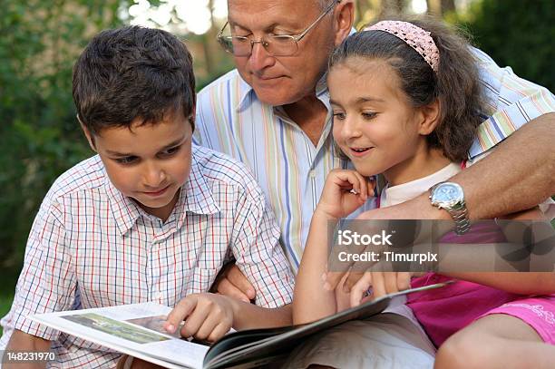 Grandfather And Kids Reading Book Outdoors Stock Photo - Download Image Now - Grandfather, Grandson, Reading
