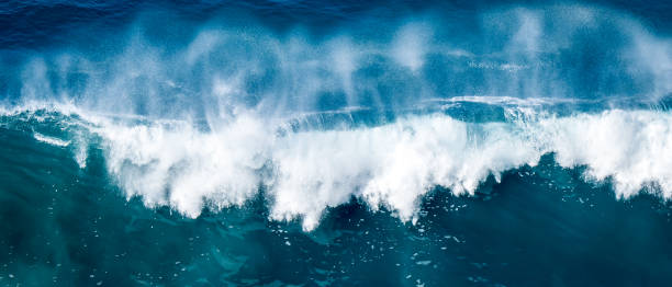 Elevated panoramic view captures the sheer power and strength of a massive breaking wave, as it crashes down with a deafening roar, sending a huge white spray high into the sky above the rough ocean.