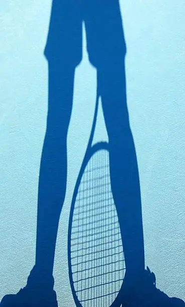 A shadow of a tennis player's legs and racquet on a blue court