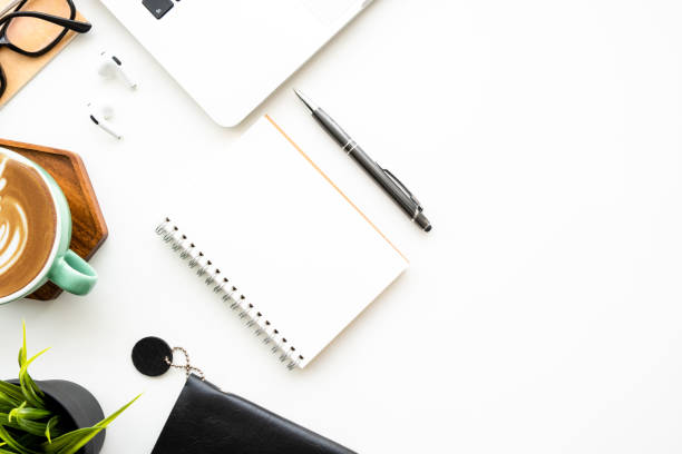 istock Blank notebook is on top of white office desk table with laptop computer and office supplies. Top view with copy space, flat lay. 1482340811