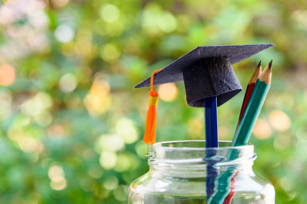 konzept des schulanfangs- oder graduiertenzertifikatsprogramms: schwarze abschlusskappe und ein bleistift in einer flasche. der schulanfang ist der zeitraum, in dem die schüler die schulunterlagen für das kommende schuljahr vorbereiten. - cap book nobody hat stock-fotos und bilder